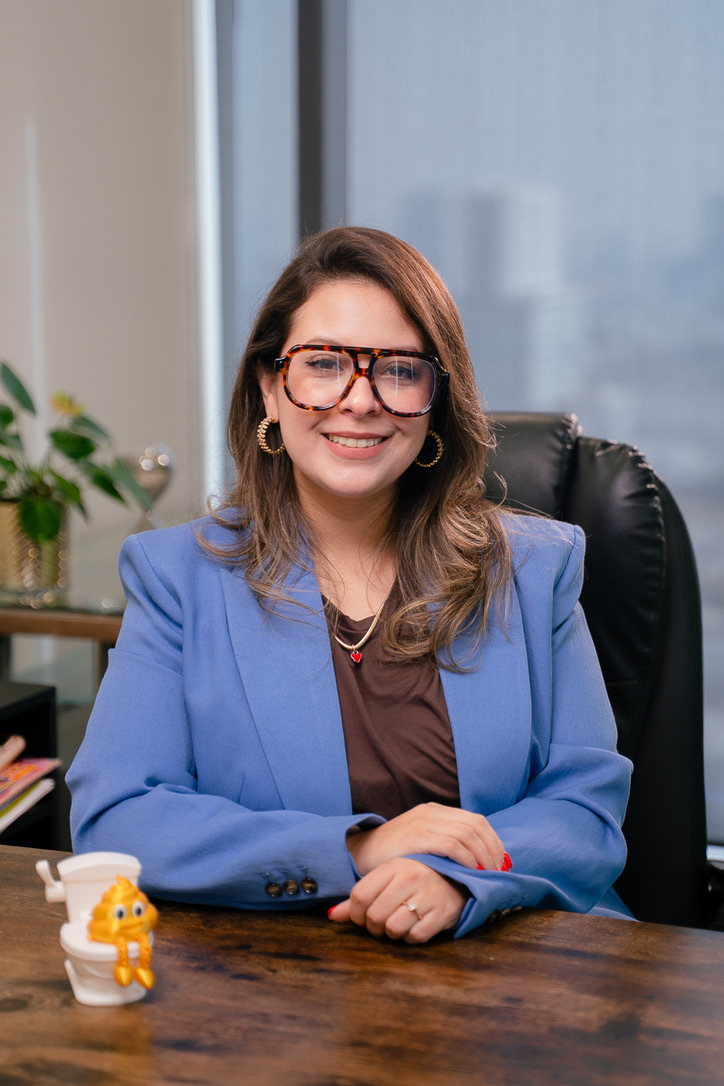 Dra. Elda Carolina Garza Dávila sentada en su consultorio, con saco azul, lentes y las manos sobre el escritorio.